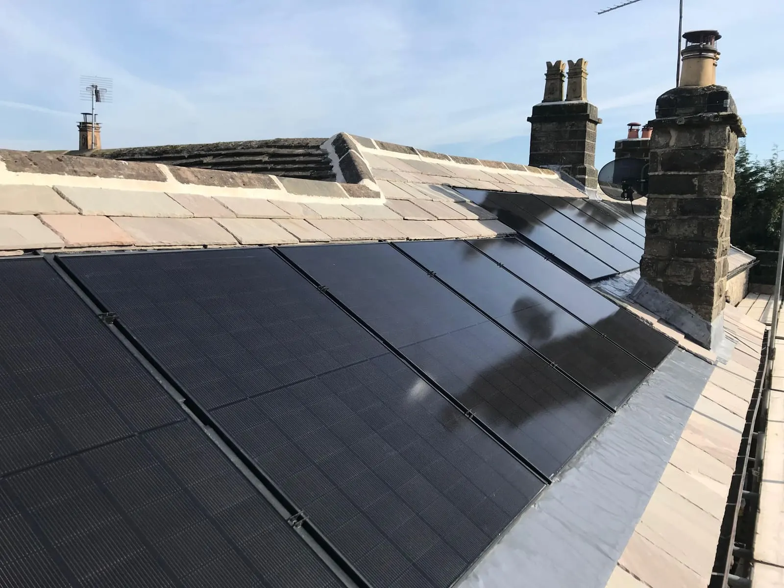 Side view of the all-black solar array running up towards the stone chimneys against a clear blue sky