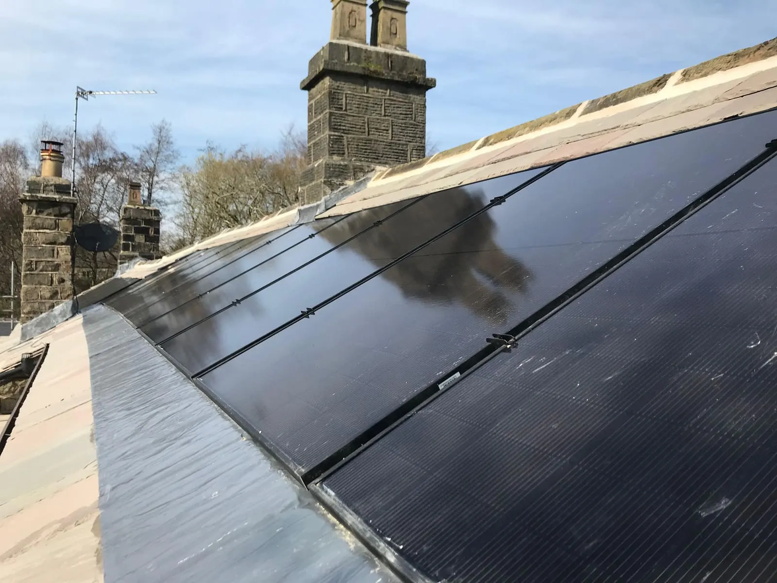 Low-angle view along the all-black solar panels and the leadwork beside the chimney