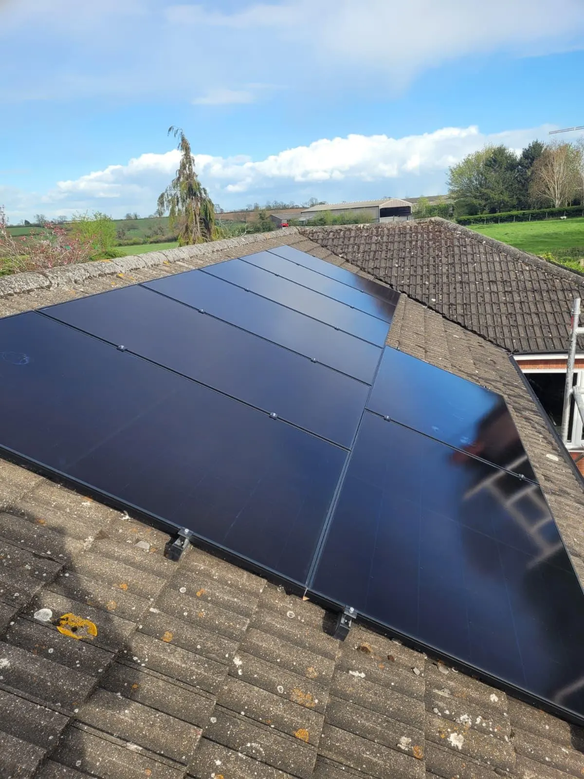 All-black solar PV array on a tiled roof with open countryside and a farm building behind