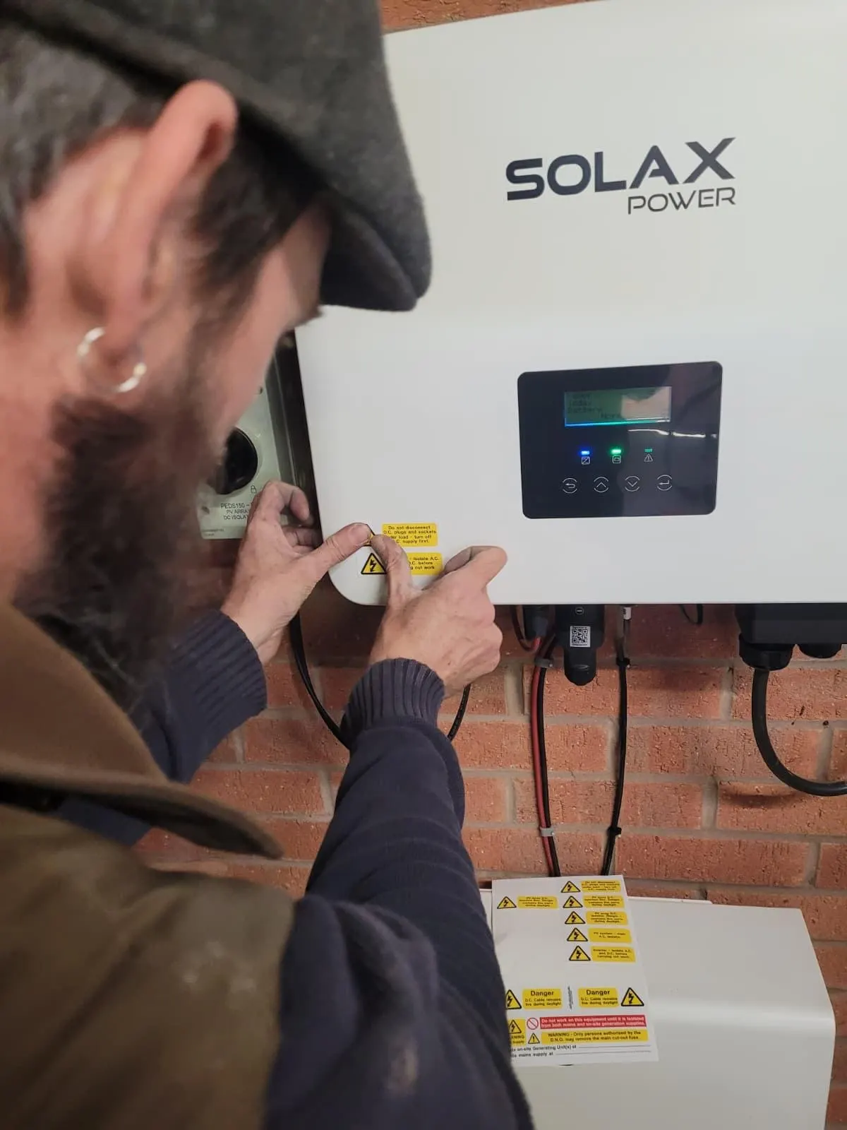 Electrician applying safety labels to a newly installed Solax Power hybrid inverter on a brick wall