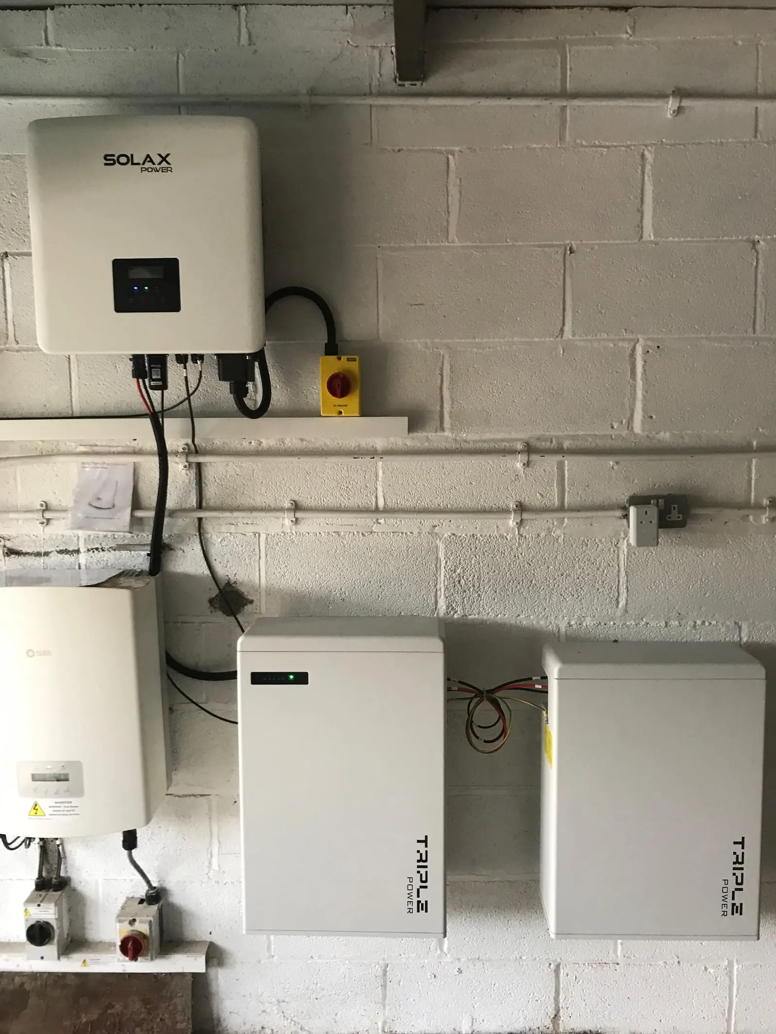 Wall-mounted Solax hybrid inverter with two Solax Triple Power battery modules and isolators on a painted wall