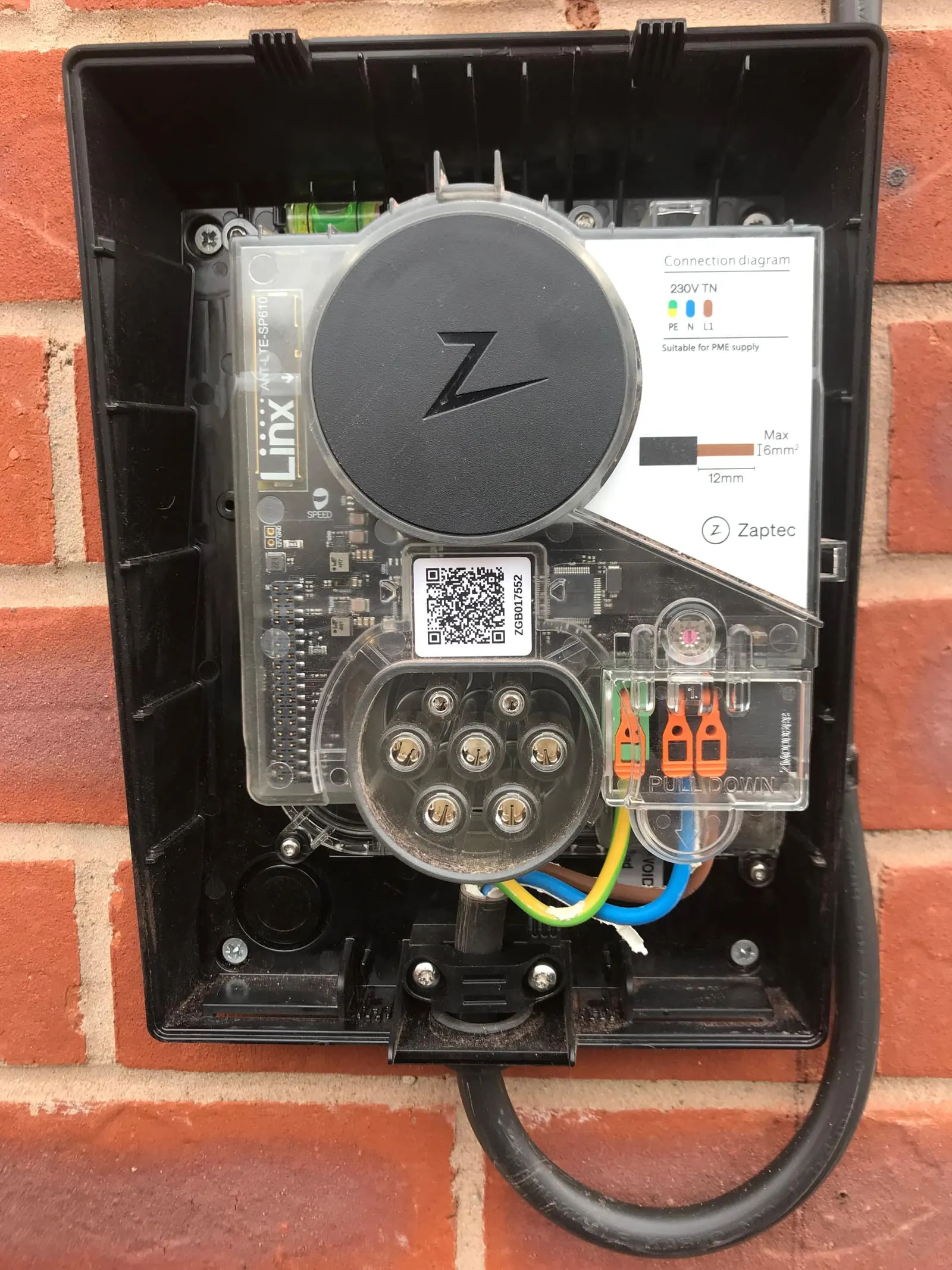 Zaptec EV charger with the cover off, showing the internal wiring and connections on a brick wall