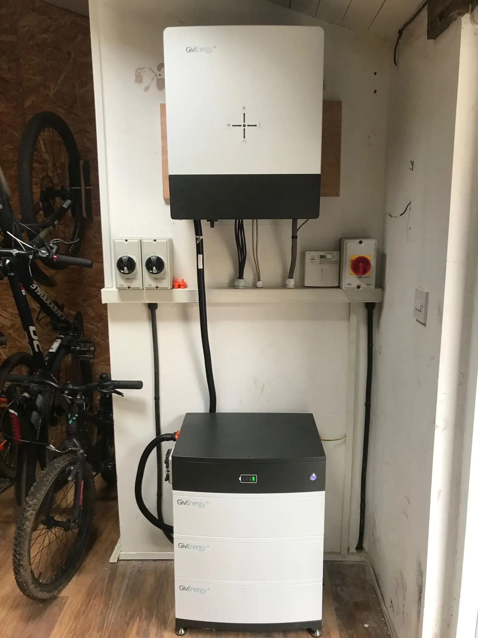 GivEnergy hybrid inverter mounted above a three-module stacked GivEnergy battery in an outbuilding